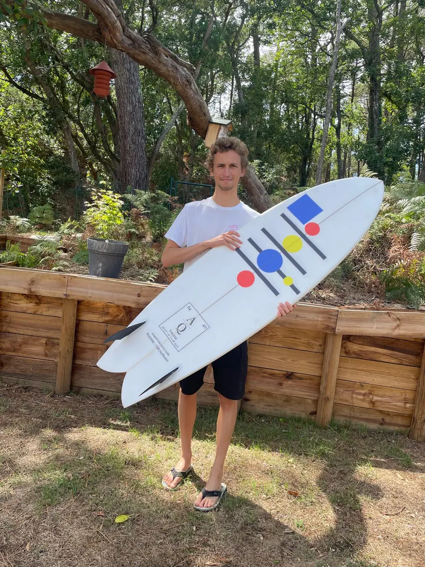 Achille debout avec sa planche fish à motifs Atomique, de face
