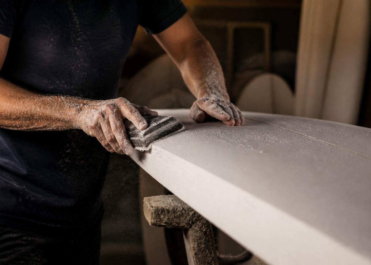 Mains d'un shaper ponçant un pain de mousse dans l'atelier